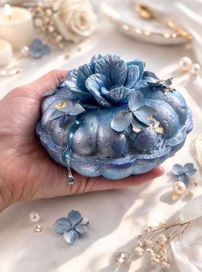 Blue decorative bath bomb resembling a flower held in a hand with a soft, blurred background