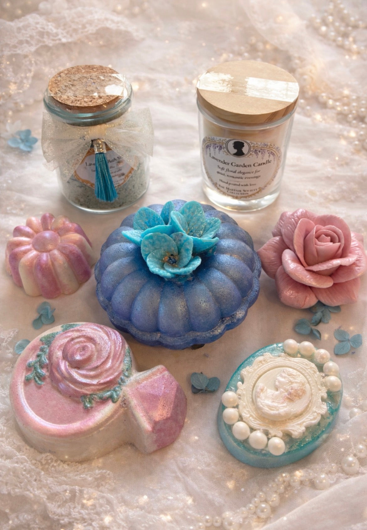 Luxury spa gift set items including bath salts, candle, bath bombs and handmade soaps arranged on lace with pearls.
