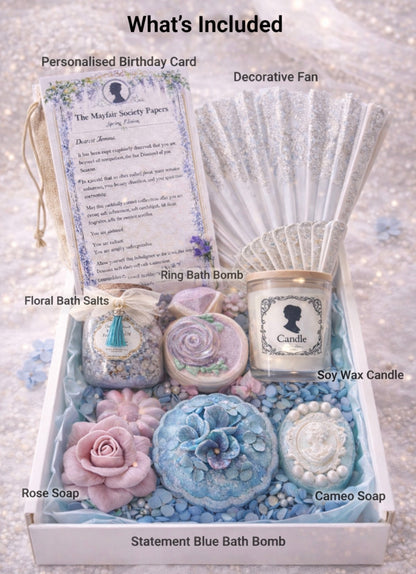 Luxury spa gift box contents including a personalized birthday card, decorative fan, bath bombs, rose soap, cameo soap and soy candles on a glittery background