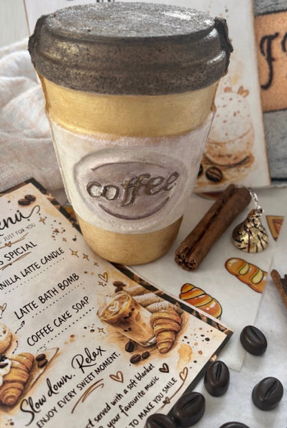 Coffee cup bath bomb with a lid on a surface with coffee-themed items and a menu.