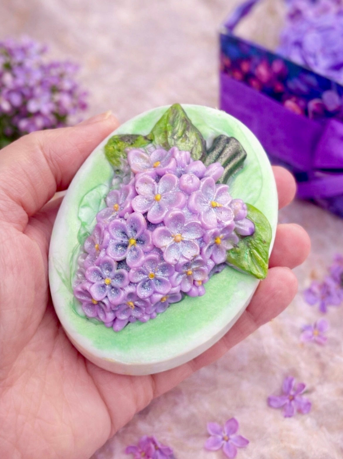Handmade lilac flower soap held in hand to show size, featuring realistic purple blossoms and green leaves, part of the Lilac Spa Gift Box for her.

