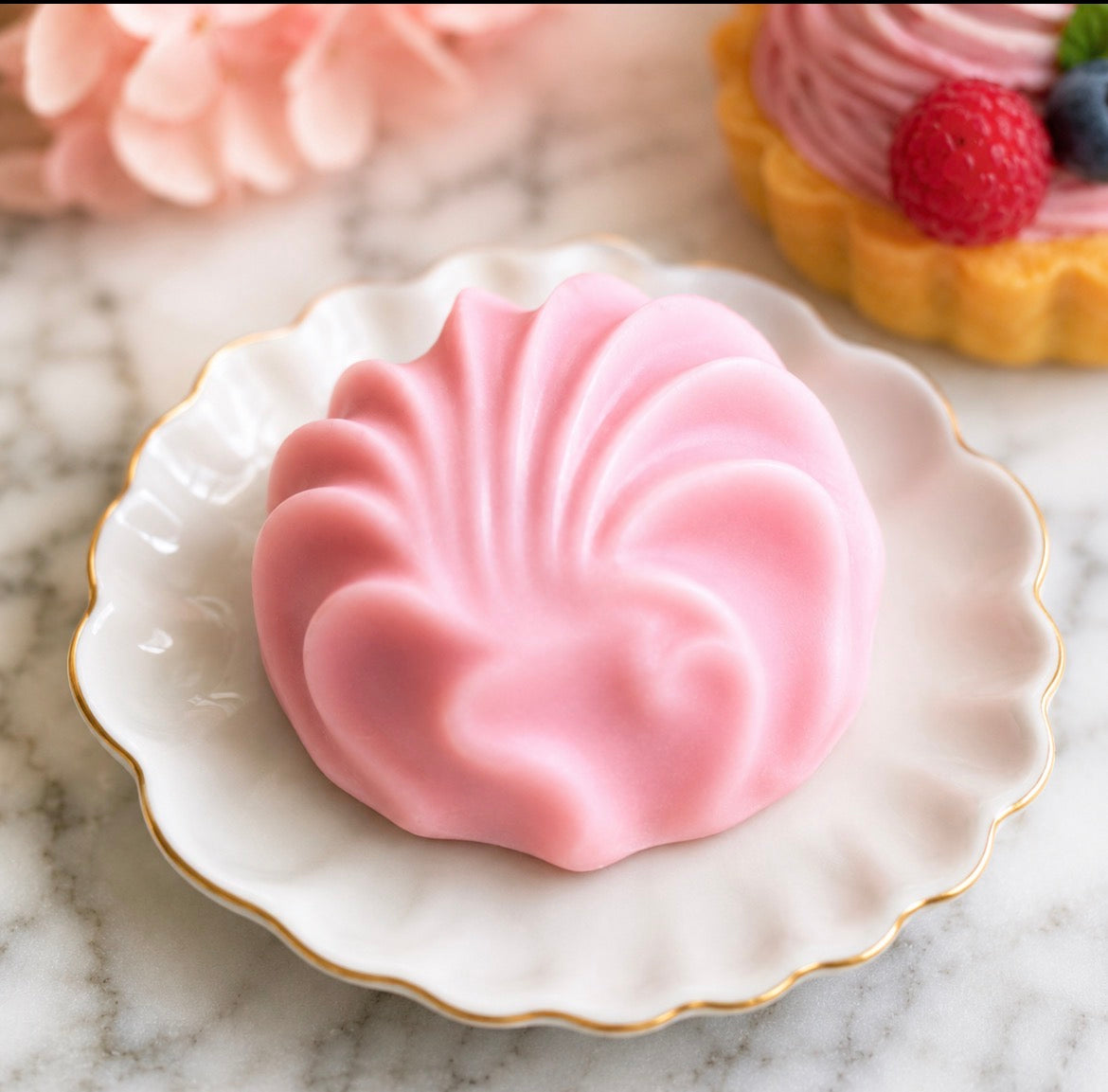 Pink shell-shaped dessert soap on a decorative plate with a marble background