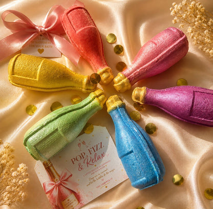 Colorful bath bomb bottles arranged in a circle on a soft fabric background with a card.