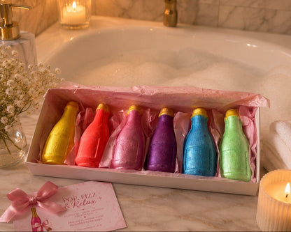 Colorful bath bomb bottles in a box with candles and flowers in the background