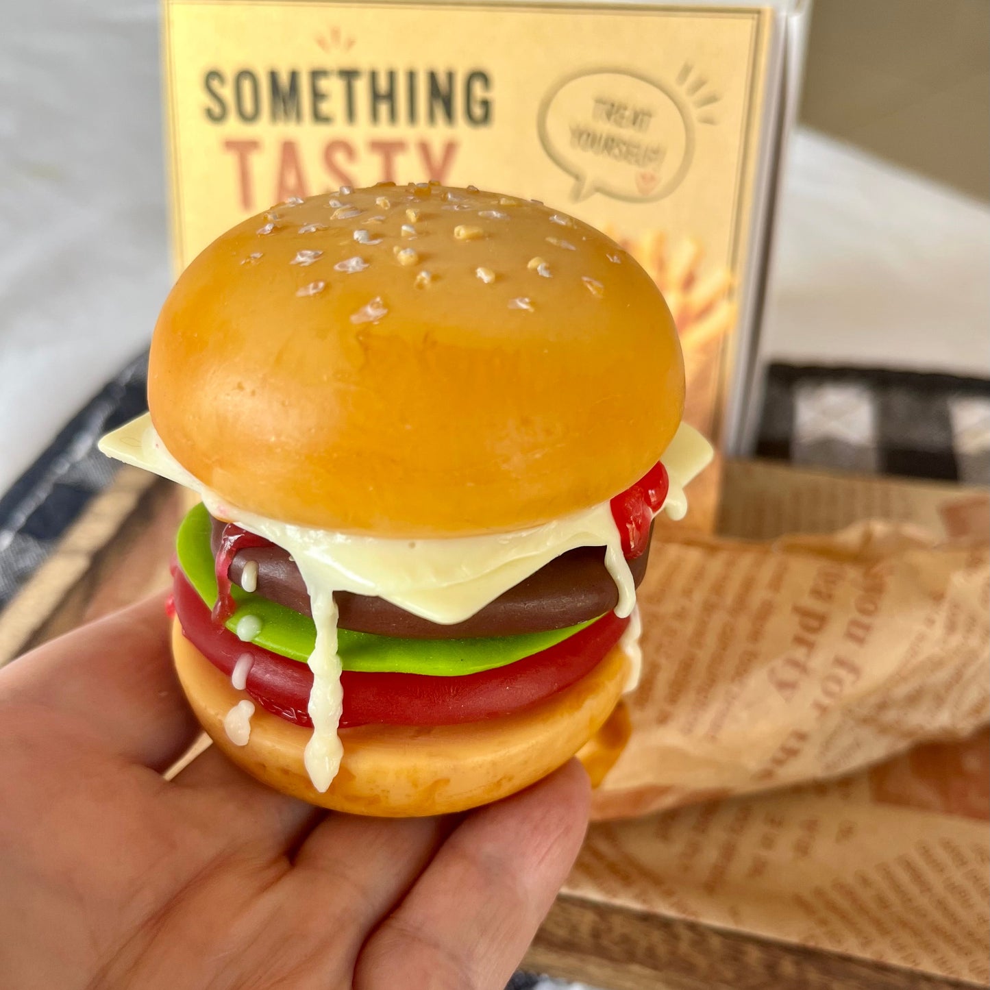 Close-up of a handmade cheeseburger soap held in a hand, showing realistic burger layers and melted cheese. Unique novelty soap gift for food lovers.