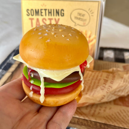 Close-up of a handmade cheeseburger soap held in a hand, showing realistic burger layers and melted cheese. Unique novelty soap gift for food lovers.