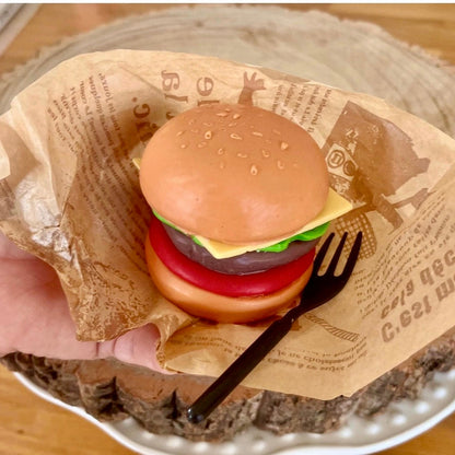 Hand holding a realistic handmade cheeseburger soap with burger layers and sesame bun. Unique novelty soap designed to look like real fast food.