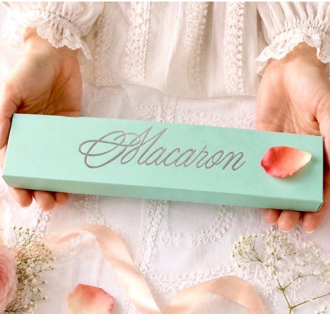 Woman holding a mint green macaron soap gift box, styled with delicate flowers, pink ribbon and rose petals.