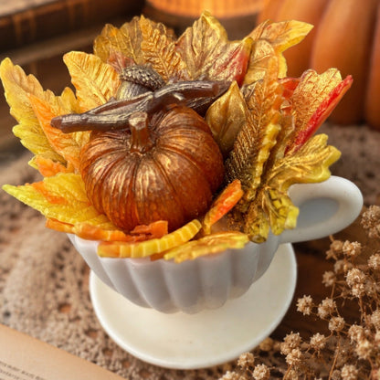 Handmade pumpkin teacup soap decorated with autumn leaves and a miniature pumpkin, displayed in a white teacup. Cozy fall gift and seasonal artisan soap